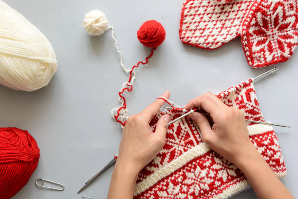 girl knits röda och vita norska jacquard mössa stickor på grå trä bakgrund. processen av stickning. ovanifrån. lekmanna-platt - knitting bildbanksfoton och bilder