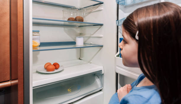 Girl looking at empty fridge due to a crisis Worried girl looking at the almost empty fridge due to a crisis hungry stock pictures, royalty-free photos & images