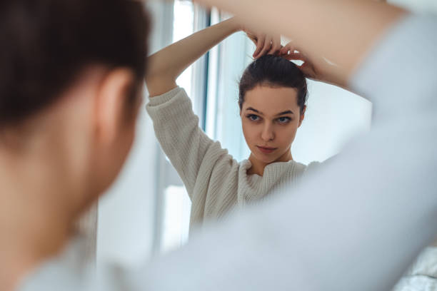 Girl looking in the mirror while making ponytail stock photo