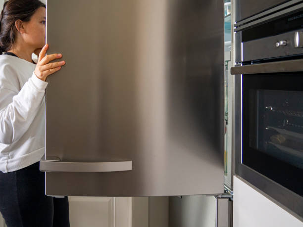 Girl looking inside an open refrigerator for food in a domestic kitchen. stock photo