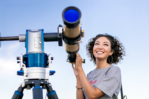 girl looking through a telescope outdoors