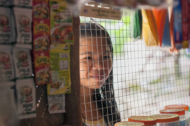 A girl looks through the grille deep into the village shop Popototan island, Philippines - January 16, 2012: A girl looks through the grille deep into the village shop philippine girl stock pictures, royalty-free photos & images