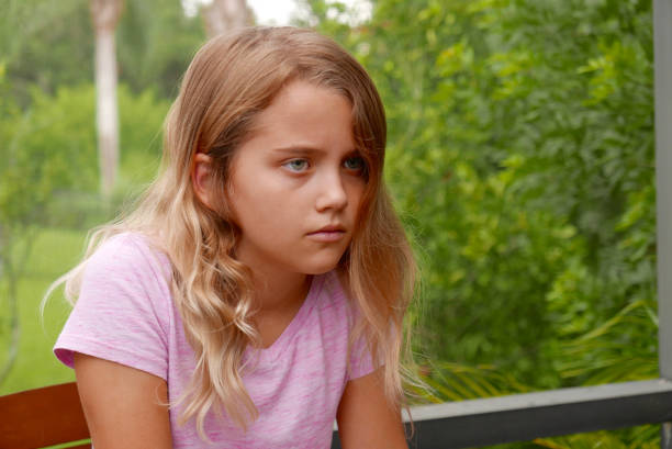 Girl outside, looking sad, with outdoor greenery in the background stock photo