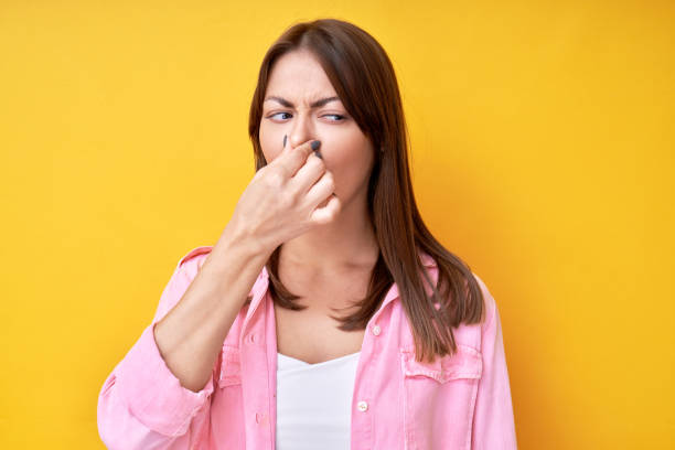 Girl pinched her nose with fingers, concept of unpleasant smell of sweat and bad breath, isolated in yellow studio stock photo