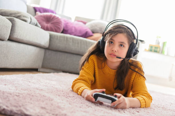 Girl playing games on a video game console A girl laying down in a living room and playing games on a video game console while using a headset with microphone. swedish girl stock pictures, royalty-free photos & images