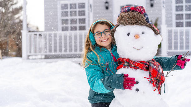 Girl playing with a snowman in front of the house stock photo