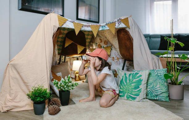 Girl playing with cardboard binoculars while camping at home stock photo
