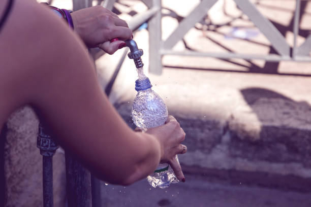 girl pours water into a bottle from street fountain with clean drinking water stock photo