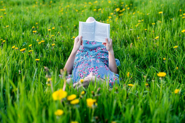 girl reading book outdoors in grass stock photo