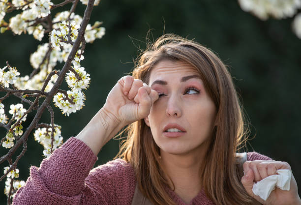 Girl rubbing eyes in front of blooming tree stock photo