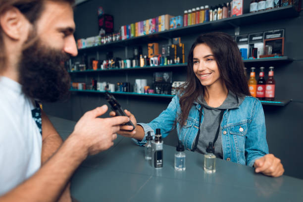 Girl seller shows the choice of electronic cigarettes in vapeshop. Girl seller shows the choice of electronic cigarettes in vapeshop. Nearby is a buyer - a man with a beard. The store has a large assortment of electronic cigarettes. little girl smoking cigarette stock pictures, royalty-free photos & images