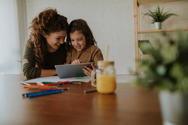 Girl showing her mom new games on her tablet. Sitting at table, taking a break from doing homework.  homework stock pictures, royalty-free photos & images