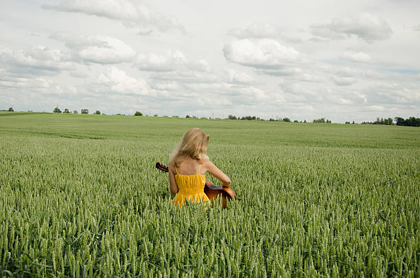 girl sit in field of rye plays guitar stock photo
