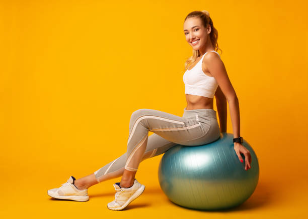 Girl Sitting On Fitball Over Yellow Background Sporty Girl Sitting On Fitball Over Yellow Studio Background. Workout And Fitness. Empty Space yoga ball work stock pictures, royalty-free photos & images