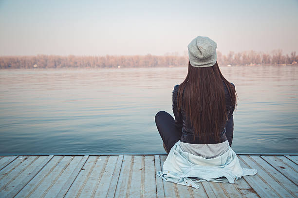 Girl sitting on pier and lookingat the river stock photo