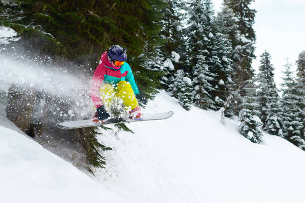 girl snowboarder jumping in the forest leaving behind spray of snow stock photo