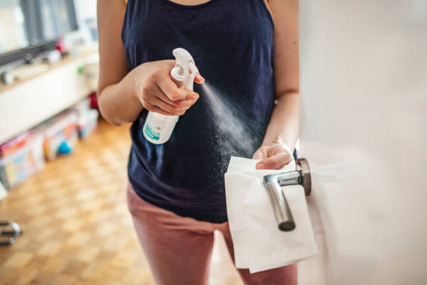 Girl staying at home during coronavirus outbreak Woman cleaning a door handle with a disinfection spray and disposable wipe. Woman sanitizing door handle with antibacterial spray. Girl staying at home during coronavirus outbreak cleaning product stock pictures, royalty-free photos & images