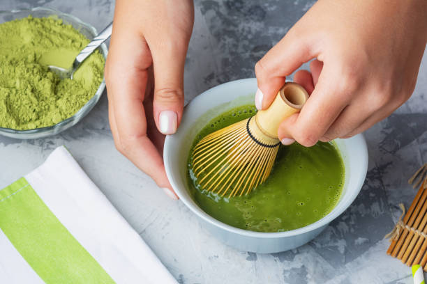 Girl stirs matcha green tea a bamboo whisk. The process of making tea close-up. stock photo