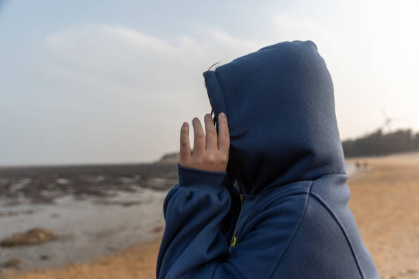 A girl stood on the beach, her face covered with her hands. stock photo
