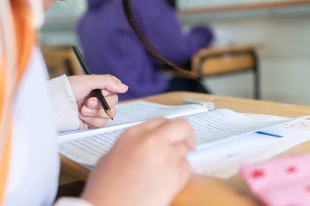 Girl Student in exam test school, Side View of high school or university holding writing document paper answer sheet and lecture final exams in classroom with white uniform pupil of Thailand stock photo