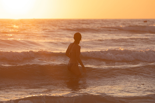 Zahara de los Atunes, Spain - Sept 09, 2021: A young and beautiful girl swims between the waves of the sea and the soft orange light of the sunset on a summer evening