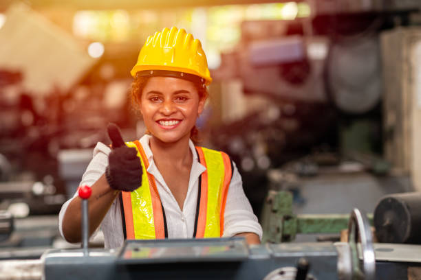 女孩青少年工人與安全帽顯示豎起大拇指工作作為勞動在工業工廠與鋼機。 - labor day 個照片及圖片檔