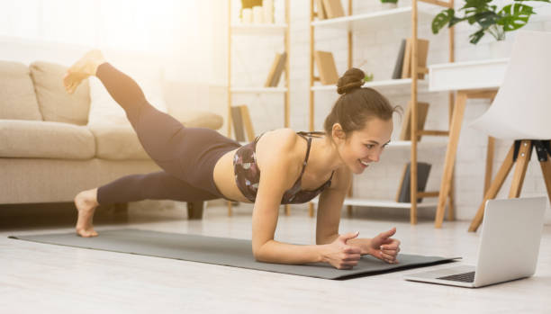 自宅で女の子のトレーニング、板やノートパソコンでビデオを見て - yoga ストックフォトと画像