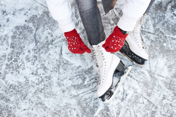 Girl tying shoelaces on ice skates before skating on the ice rink, hands in red knitted gloves. stock photo