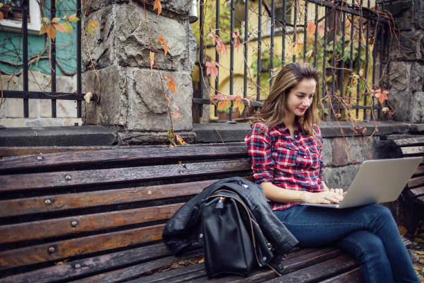 Girl using laptop Young woman texting on her laptop on a bench in the street Portable DVD Player stock pictures, royalty-free photos & images