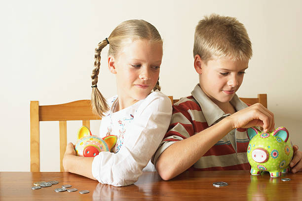 Girl (10-12) watching twin brother drop coin into piggy bank  allowance stock pictures, royalty-free photos & images