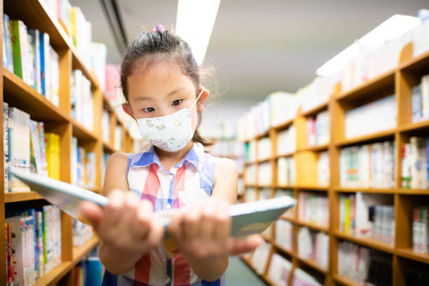 Girl wearing a mask chooses a book Girl wearing a mask chooses a book library stock pictures, royalty-free photos & images