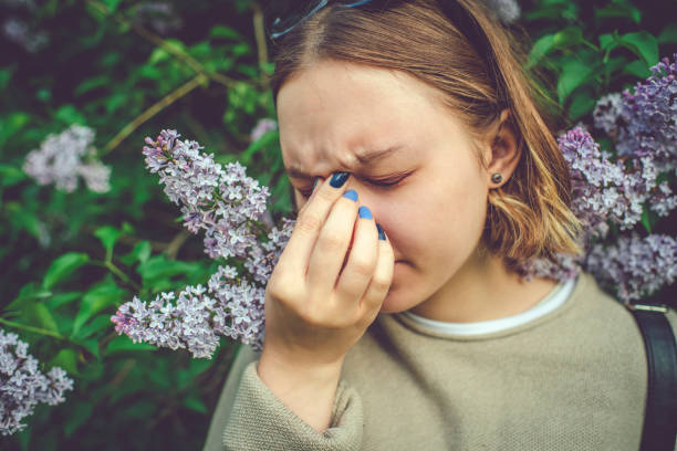 Girl with allergy sneezing and cleaning nose in park near blooming flowers in springtime Allergic teenage girl cleaning nose in park sinusitis stock pictures, royalty-free photos & images
