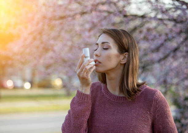 Girl with asthma pump in front of blooming tree in spring stock photo