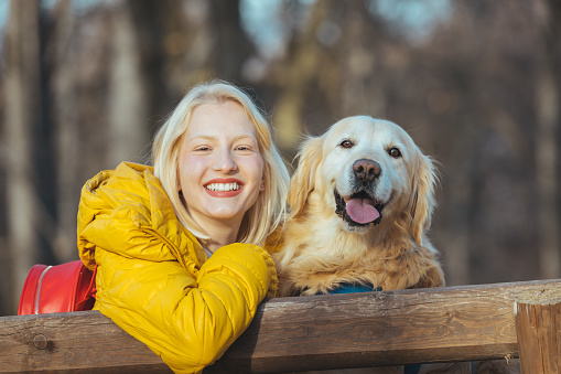 Portrait of young beautiful woman in yellow jacket sitting in the forest hugging golden retriever dog. Girl with dog. Happiness and friendship. Pet and woman. Woman playing with dog