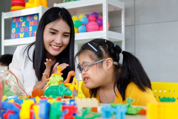 Girl with Downs syndrome play toy. Asian girl with Downs syndrome play toy with her teacher in classroom. Concept disabled kid learning. down syndrome stock pictures, royalty-free photos & images