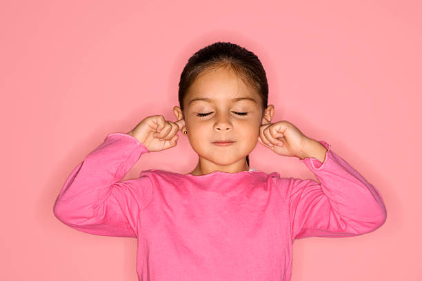 Girl with fingers in ears. Hispanic girl with fingers in ears and eyes closed against pink background. Fingers in Ears stock pictures, royalty-free photos & images