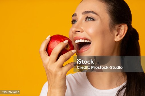 istock Girl With Perfect White Smile Holding Apple On Yellow Background 1165263287