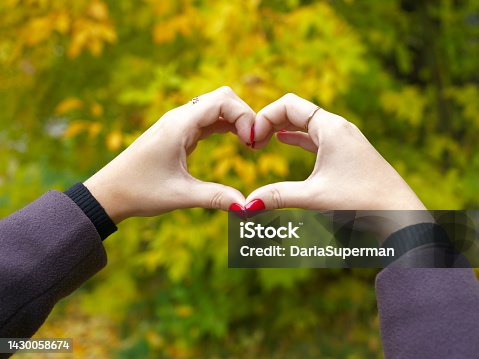 istock A girl with red manicure fingers shows a heart on a blurry autumn background. expression of sympathy. 1430058674
