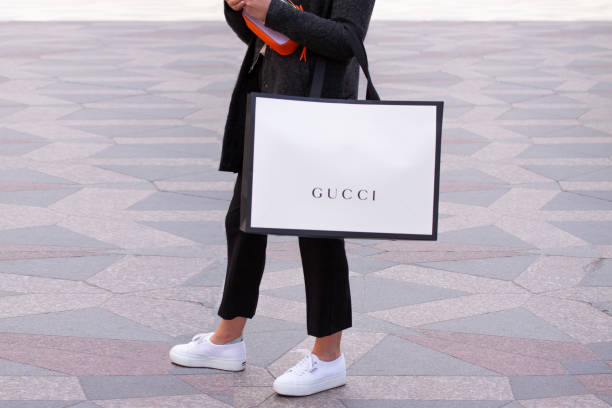 Girl with white sneakers standing holding a Gucci shopping bag on a street. Girl with white sneakers standing holding a Gucci shopping bag on a street. Copenhagen, Denmark - May 4, 2019 brand name stock pictures, royalty-free photos & images