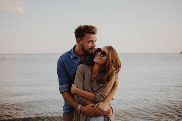 Girlfriend feeling safe in her boyfriends arms Modern couple on the beach hugging and loving each other falling in love stock pictures, royalty-free photos & images