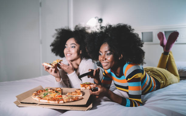 vriendinnen die pizza in bed eten en tv letten - watching tv stockfoto's en -beelden