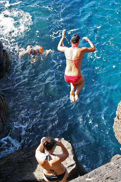 Girls Cliff Jumping into the Deep Blue "On a bright sunny day, young ladies are cliff jumping into the cool blue water off Maui. A snorkler watches in awe.Feel free to add this image to your lightbox and please view my portfolio for more cliff diving images such as these:" cliff jumping stock pictures, royalty-free photos & images