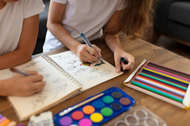 girls drawing at table with colorful pencils, spending time together stock photo