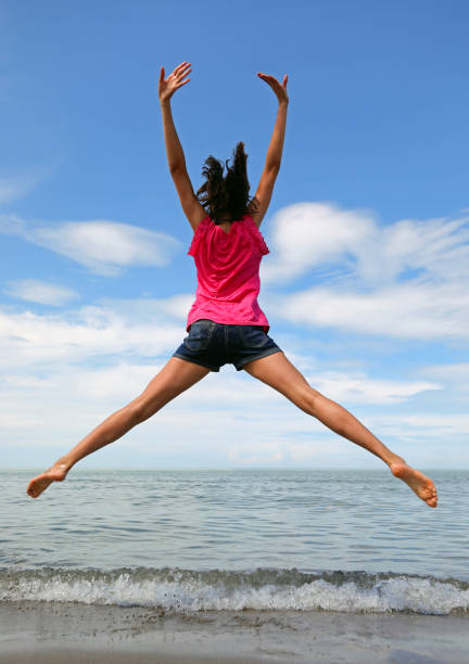 girls effect a big jump with open arms and legs by the sea in summer stock photo