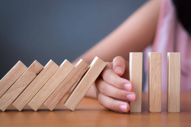 Girl's hand Stopping Falling wooden Dominoes effect from continuous toppled or risk. Girl's hand Stopping Falling wooden Dominoes effect from continuous toppled or risk, strategy and successful intervention concept for business and education. boundary stock pictures, royalty-free photos & images