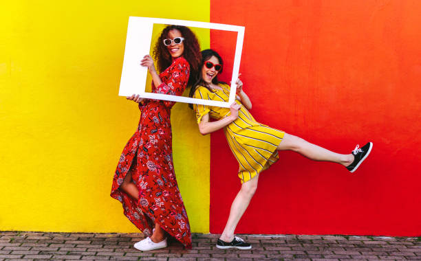 Girls posing with empty picture frame Two women friends with blank photo frame standing against colored wall outdoors. Female travelers posing at camera with empty picture frame. female friendship photos stock pictures, royalty-free photos & images