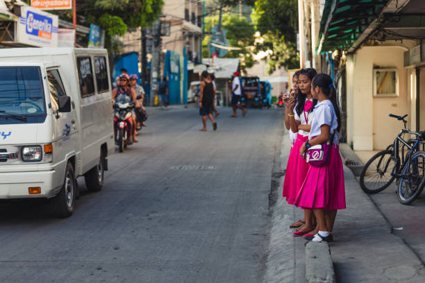 Girls waiting to cross a street to go to school Malay, Philippines - January 11, 2016: Three girls in school uniforms, waiting to cross a street in Boracay island, on the municipality of Malay, Philippines. filipino family stock pictures, royalty-free photos & images