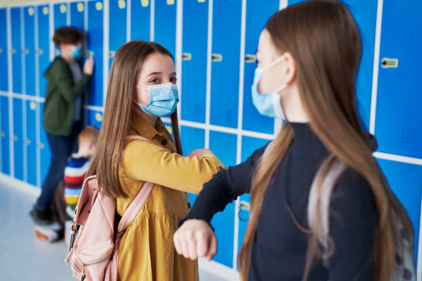 Girls wearing protective masks and having an elbow greeting stock photo