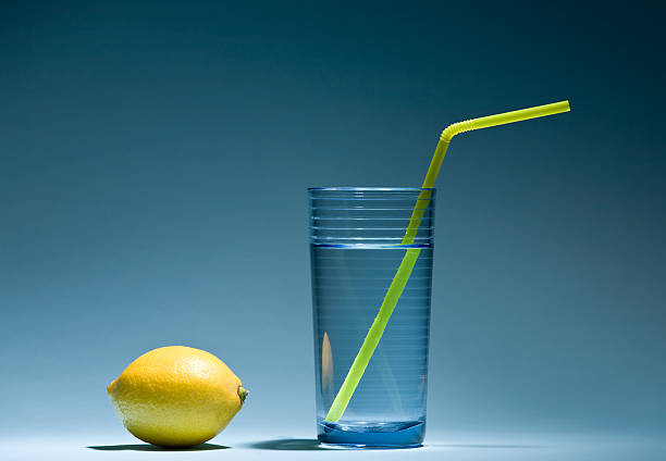 Lemon and glass of water with yellow straw close-up.