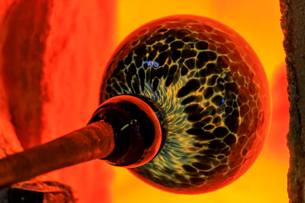 Glass blower working on a bubble of melted glass on a rod by heating it up in a kiln at a glass maker's workshop stock photo